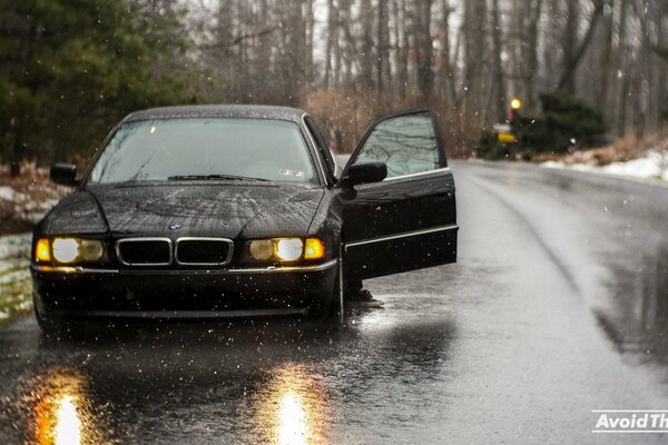 There is a black boomer on the autumn street, the headlights are reflected in the wet asphalt