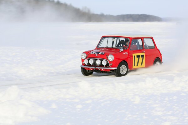 A red car is driving through the snow