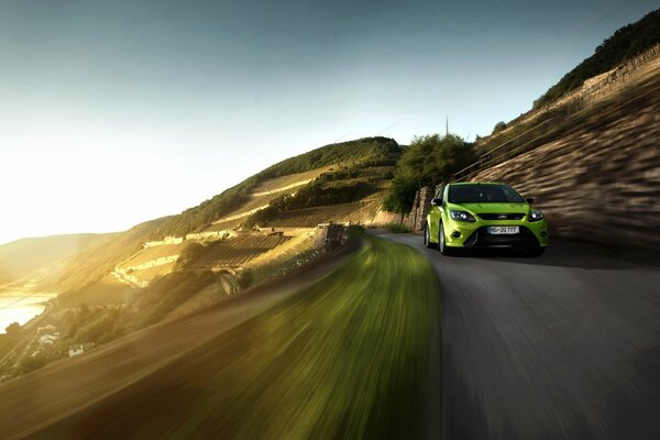 Ford Focus vert clair en mouvement au coucher du soleil, le long des montagnes