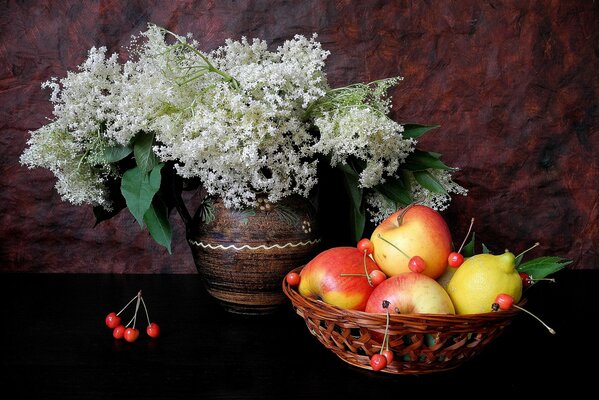 On the black table there is a vase with lilacs and a basket with apples