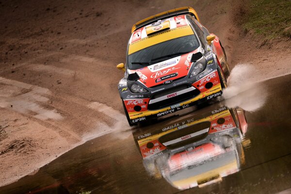 A sports car drives through a large puddle during a race