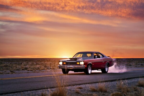 The car is driving on the road against the background of sunset