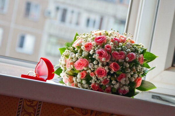 Bouquet de mariage de roses et bagues de fiançailles dans une boîte sur le rebord de la fenêtre