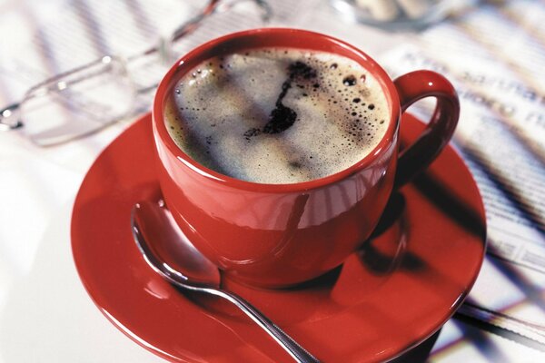 Una taza de café en una taza roja de pie en el periódico de la mañana