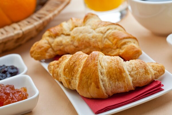 A couple of croissants on a napkin with saucers of jam standing next to it