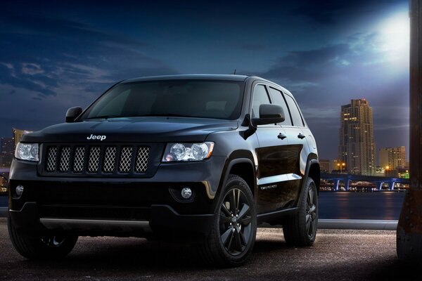 Coche jeep grand cherokee por la noche en el fondo de la ciudad y la Luna brilla