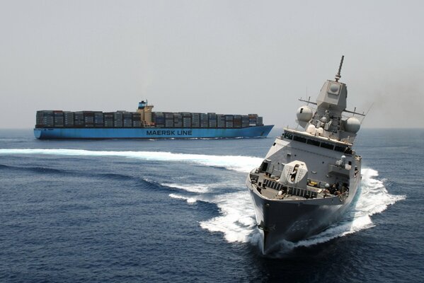 Manövrierende Militärfregatte im Meer vor dem Hintergrund eines Containerschiffes