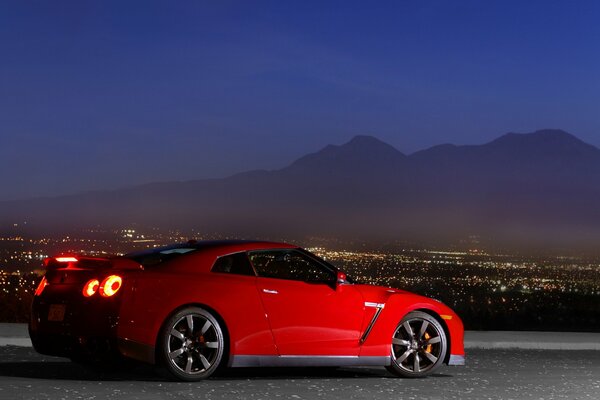 Una Nissan rossa si trova sullo sfondo di una città serale di profilo