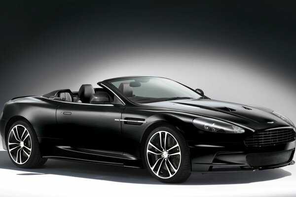 La decappottabile nera Aston Martin su sfondo grigio è illuminata da una luce bianca