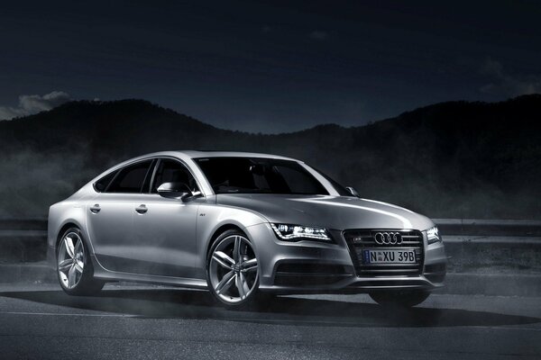 Audi A7 grigio su sfondo scuro con montagne