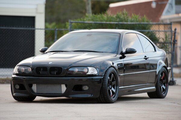 A black BMW without license plates stands against the fence