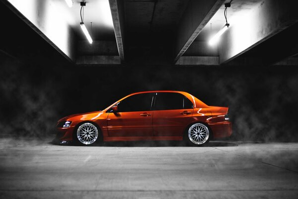 A low orange car on a concrete floor in the rays of lamps on a black background