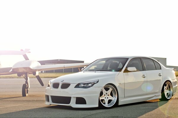 Blanco hermoso coche m5, E60 se encuentra en el campo de aviación al lado del maíz avión