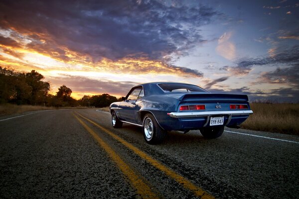 The car is driving along the road towards sunset