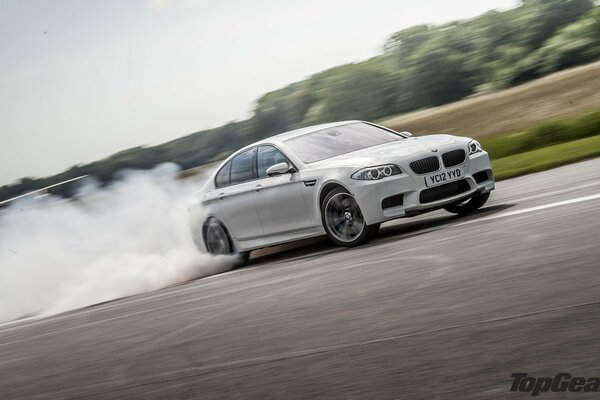 A white BMW is moving in a skid on the asphalt