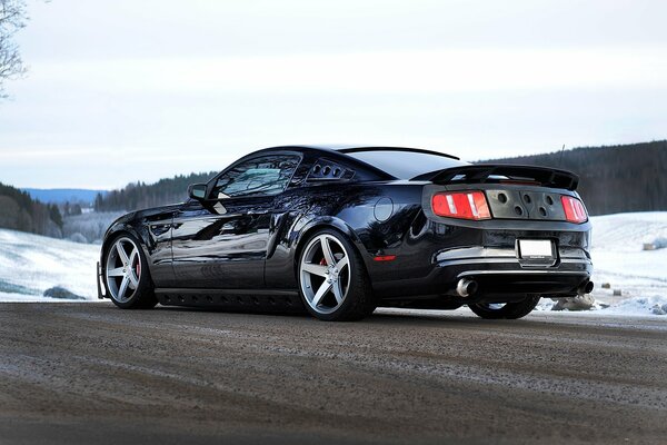 Czarny Ford Mustang na zimowej drodze