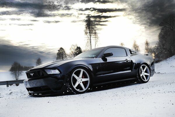 Ford Mustang nera sullo sfondo del paesaggio invernale
