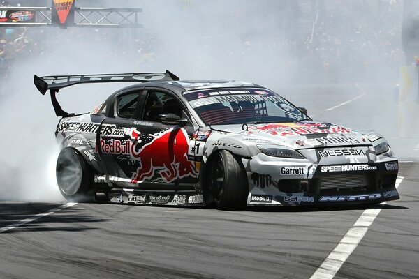 A sports mazda with an advertisement for a red bull drink is drifting on the highway