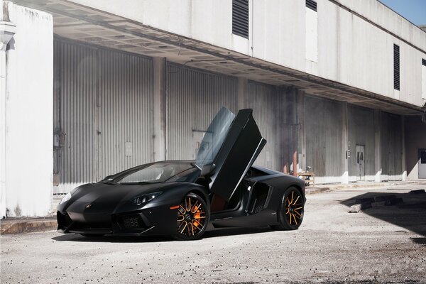 A black Lamborghini with an open door on the background of an abandoned warehouse