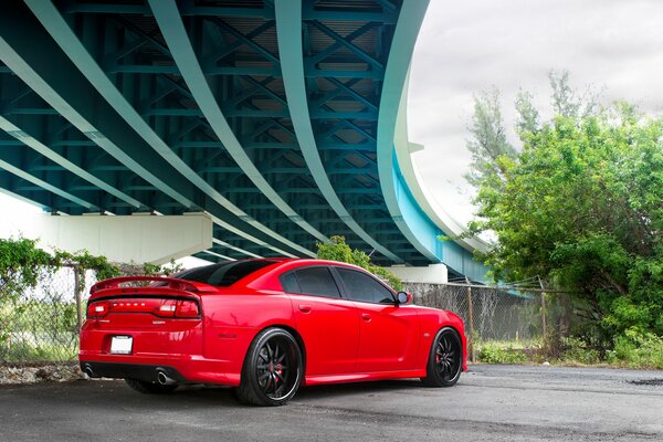 A red sportian car stands under a modern concrete bridge, rear view