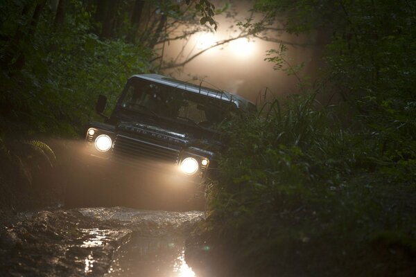 SUV im Wald im Schlamm mit eingeschalteten Scheinwerfern