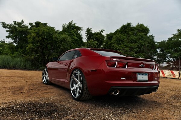 A red Chevrolet is parked on the sand near the trees