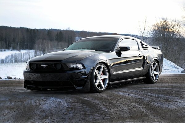 A black Ford Mustang on the road near a snowy forest