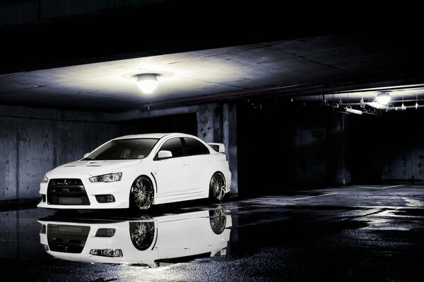 Mitsubishi Evolution blanco bajo una linterna con un reflejo en un charco