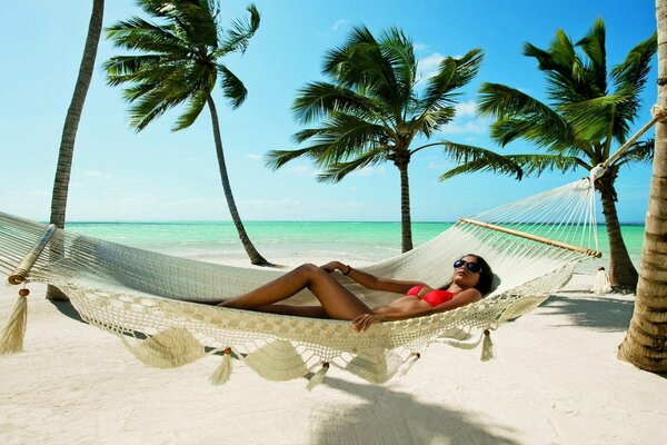 A beautiful girl in a swimsuit is lying in a hammock