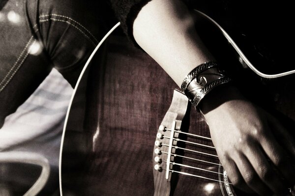 Hand mit Armband auf den Stühlen auf der Gitarre