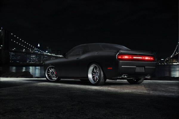 Dodge Challenger nero sullo sfondo di una metropoli con un ponte