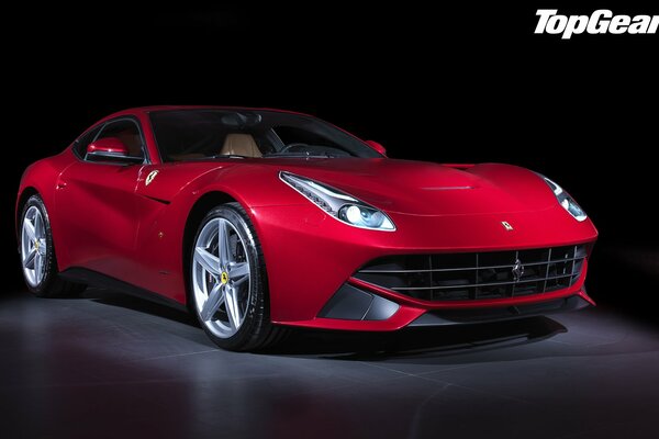 A red Ferrari F12 berlinetta stands in the semi-darkness