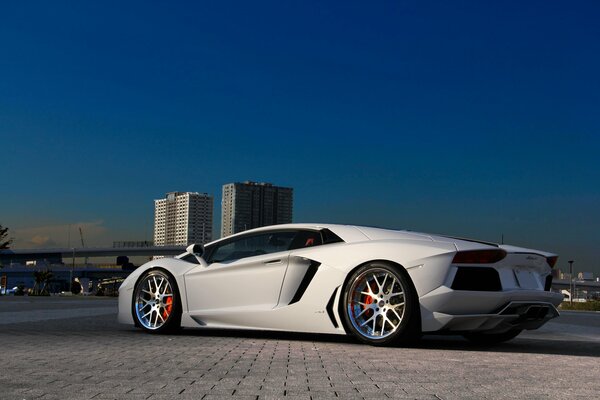 Snow-white Lamborghini against the background of tall buildings made of blue sky