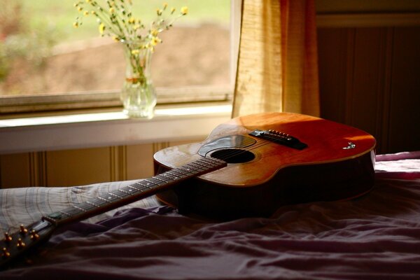 Gitarre auf der Krippe und Vase mit Blumen auf dem Fenster