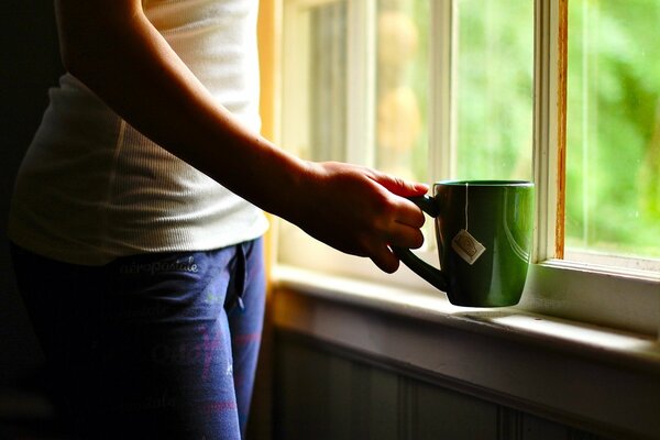 A green cup of tea in his hands by the window