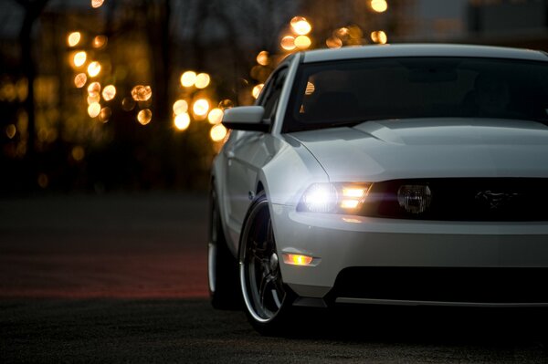 Weißer Ford Mustang fährt am Abend die Straße entlang