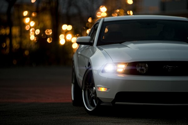 Un Ford Mustang blanco monta en la carretera por la noche