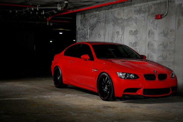 A red Bmw M3 is parked in an underground parking lot