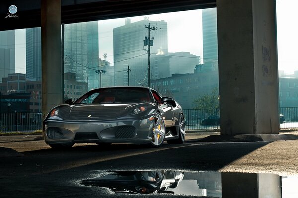 Coche Ferrari de metal plateado en un edificio abandonado en medio de rascacielos