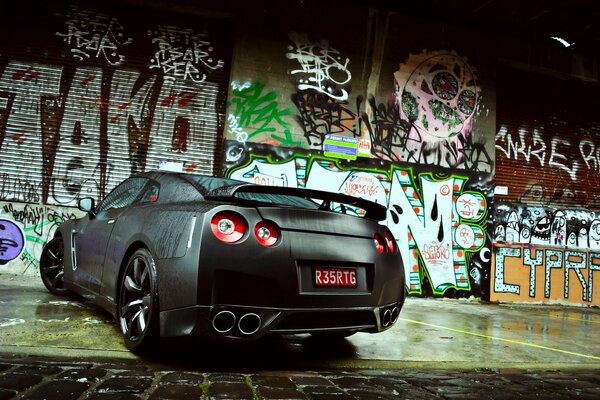 A gray nissan stands against a graffiti wall