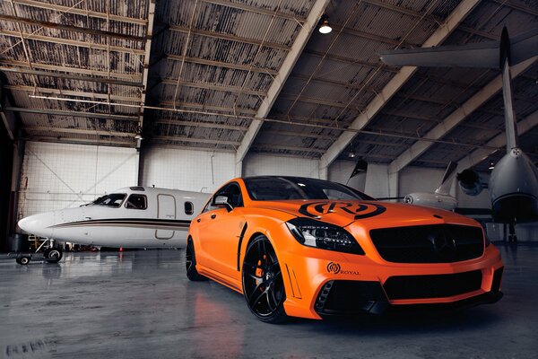 Orange Mercedes in an aircraft hangar with an airplane