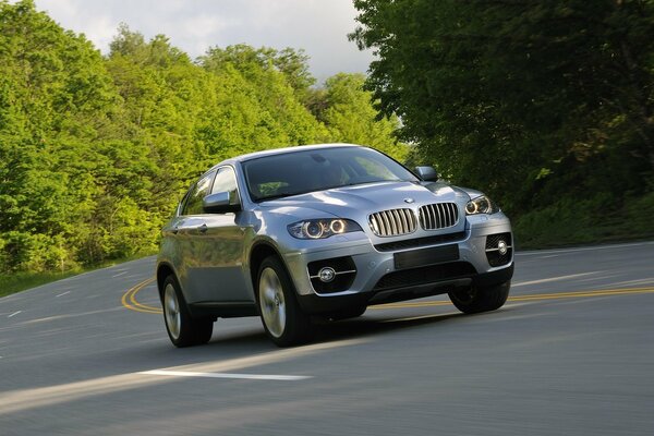 BMW ix6 is driving along the road near the trees