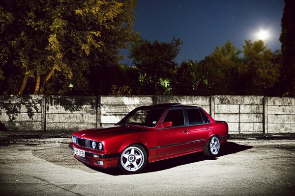 Red BMW e30 on the background of a night fence under the moon
