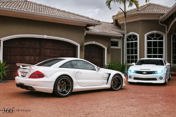 A muscle car Camaro and an elegant Mercedes are standing near the house