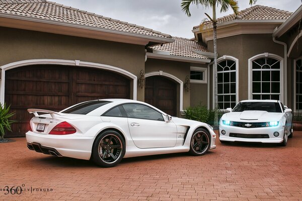 Muscle car Camaro i elegancki Mercedes stoją w pobliżu domu