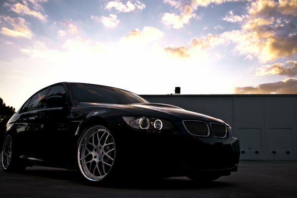 A black BMW stands against the background of clouds