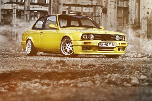 Żółte zaniżone BMW Serii 3 E30 na tle ruin