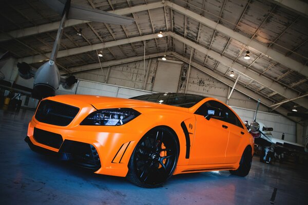 Orange mercedes-benz in a hangar with an airplane