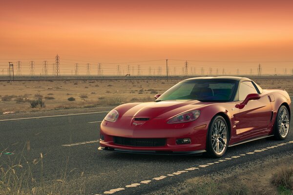 Corvette rojo monta al atardecer en la carretera