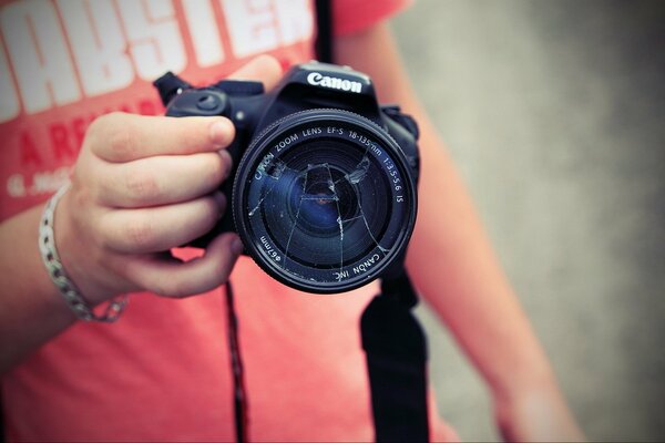 A hand holds a camera with a broken glass